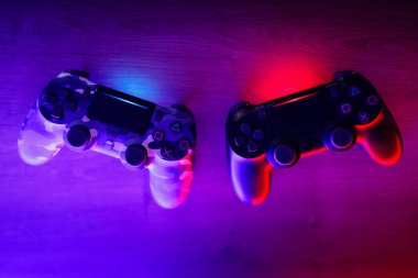 Two gamepads on a wooden table with red and blue backlight.