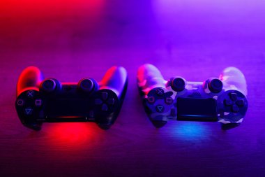 Two gamepads on a wooden table with red and blue backlight.