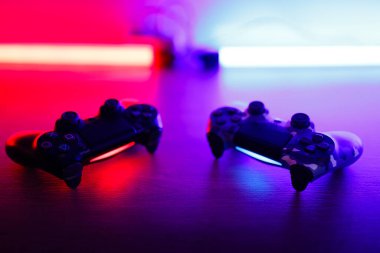 Two gamepads on a wooden table with red and blue backlight.