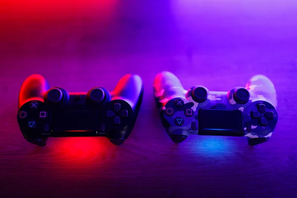 stock image Two gamepads on a wooden table with red and blue backlight.