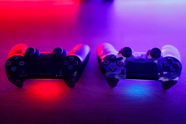 stock image Two gamepads on a wooden table with red and blue backlight.