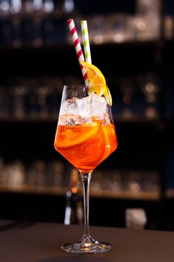 Orange cocktails with ice cubes and straws on the bar counter, on a dark background