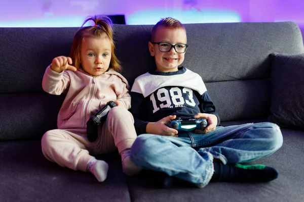 Older brother teaches younger sister to play the console. Children are emotionally happy when they win and sad when they lose.