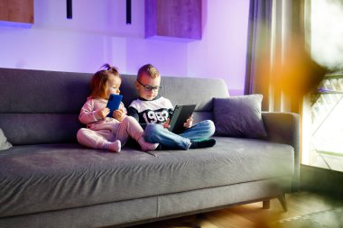 Danya and his younger sister Emilia play with mobile phones and tablets. Children are constantly sitting on phones and tablets.
