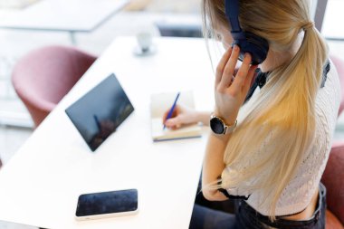 Kız uzaktan tablet üzerinde çalışıyor ve bir not defterine bilgi yazıyor.