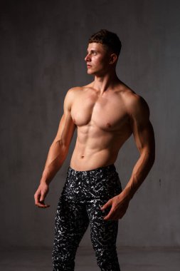 Vücut geliştirici stüdyoda. Dambılları ve gri arka planda çıplak gövdesi olan sandalyeleri var..