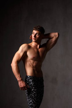 Vücut geliştirici stüdyoda. Dambılları ve gri arka planda çıplak gövdesi olan sandalyeleri var..