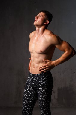 Vücut geliştirici stüdyoda. Dambılları ve gri arka planda çıplak gövdesi olan sandalyeleri var..