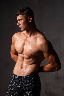 Vücut geliştirici stüdyoda. Dambılları ve gri arka planda çıplak gövdesi olan sandalyeleri var..