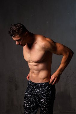 Vücut geliştirici stüdyoda. Dambılları ve gri arka planda çıplak gövdesi olan sandalyeleri var..