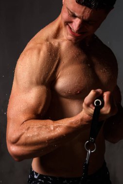 Vücut geliştirici stüdyoda. Dambılları ve gri arka planda çıplak gövdesi olan sandalyeleri var..