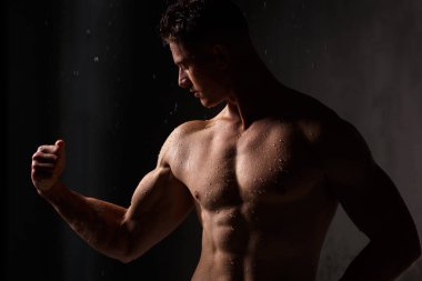 Vücut geliştirici, yağmurda stüdyoda kaslarını ve figürlerini sergiliyor..