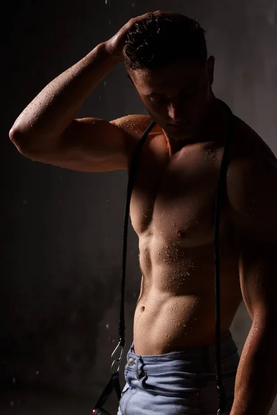 ボディビルダーは彼の筋肉と雨の中でスタジオでフィギュアを誇示します — ストック写真