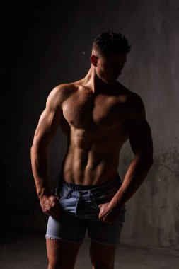 Vücut geliştirici, yağmurda stüdyoda kaslarını ve figürlerini sergiliyor..