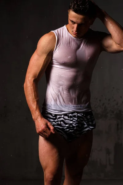 ボディビルダーは彼の筋肉と雨の中でスタジオでフィギュアを誇示します — ストック写真