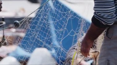 Balıkçı rıhtımdaki balıkçı teknesinde balık ağlarını tamir ediyor.