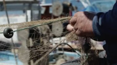 Balıkçı rıhtımdaki balıkçı teknesinde balık ağlarını tamir ediyor.