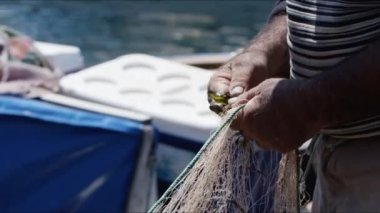 Balıkçı rıhtımdaki balıkçı teknesinde balık ağlarını tamir ediyor.