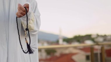 Beyaz elbiseli kadın tespih ve camiyle namaz kılıyor.
