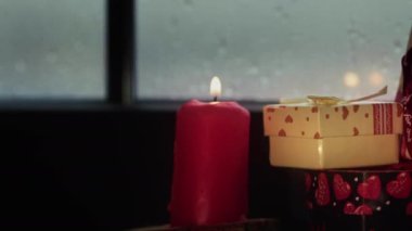 Kutsal Noel arifesi dekorasyon kutlaması ve hediye kutuları mum ışığında yağmurlu bir günde pencere camının yanında.
