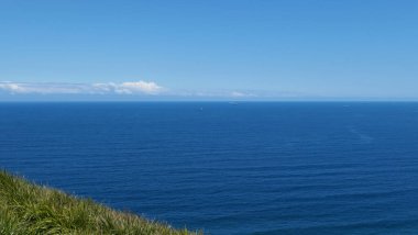 Önünde çimen üçgeni ve tepesinde bulutlar olan sakin mavi denizin genel arka planı. Yüksek kalite fotoğraf