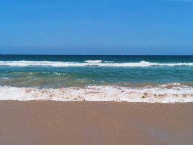 Ön planda kum, yana kayalar ve arka planda dalgalar olan güzel bir plaj sahnesi. Yüksek kalite fotoğraf