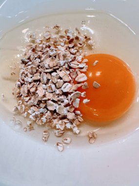 Raw egg in white dish with uncooked porridge oats clipart