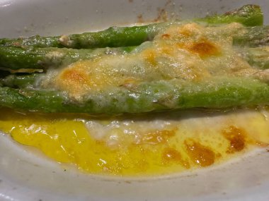 Beyaz tabakta erimiş parmesan peynirli kuşkonmaz mızrakları. Doymuş yağ oranı yüksek.