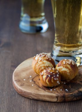 Arkasında bira bardakları olan ahşap bir tahtanın üzerinde üç ev yapımı pretzel nugget.. 