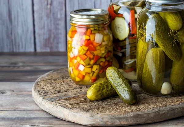 A close up of jars of pickles and peppers against a wooden background.