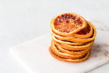 Bir yığın kurutulmuş portakal dilimleri tarçın ve şeker ile baharatlı, beyaz arka planda.