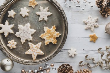 Dekorasyonlarla çevrili eski bir tabakta dezenfekte edilmiş yıldız ve kar tanesi şekilli şeker kurabiyeleri.