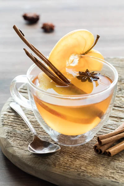 A tea cup filled with hot apple cider and garnished with a cinnamon stick, apple slice and star anise.