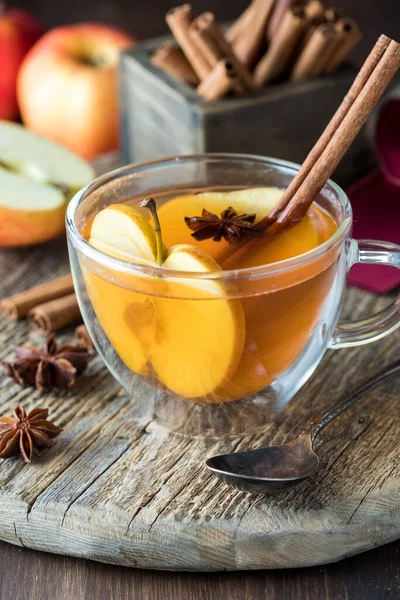 Hot apple cider in a tea cup garnished with a cinnamon stick, star anise and apple slices.