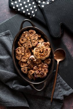 Fırından yeni çıkmış kavrulmuş sarımsak soğanları siyah bir tahta üzerinde tepeden tırnağa görülüyor.. 