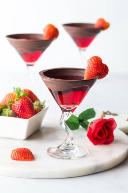 Bright red Valentines Day cocktails with chocolate dipped rims and garnished with heart shaped strawberries 
