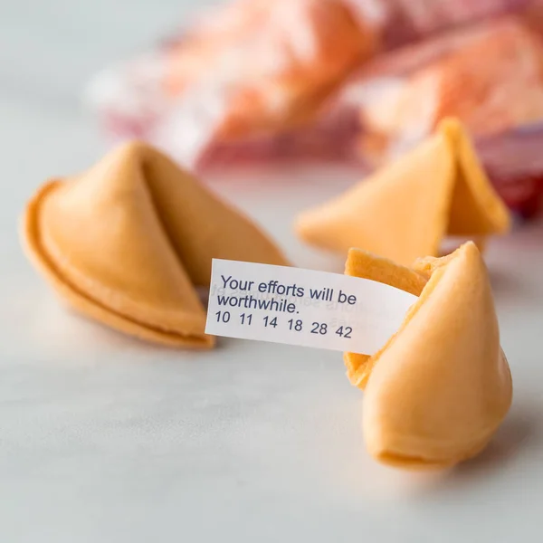 A close up of a fortune cookie with a fortune note inserted and sticking out with other cookies in behind.