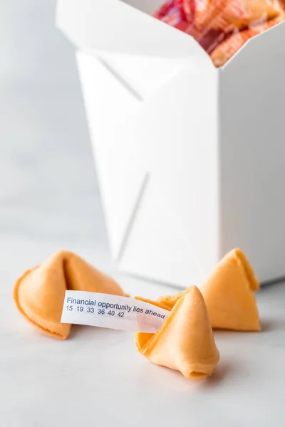 A cardboard box of fortune cookies with a fortune note sticking out of the one in front.