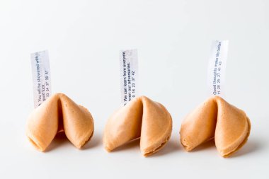 Three whole crispy fortune cookies in a row with fortune notes inserted and sticking straight up.