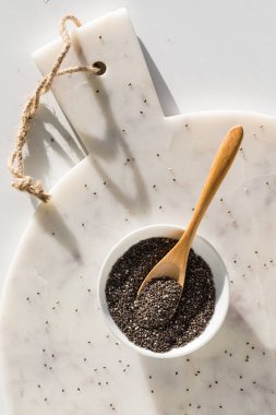 Top down view of a bowl of chia seeds on a white marble board in bright sunlight. 