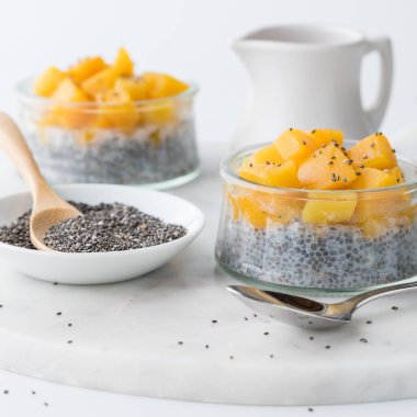Two chia pudding parfaits topped with diced mangos and a bowl of chia seeds beside.