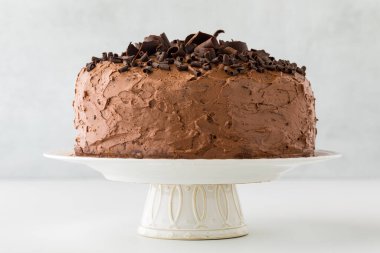 A whole triple layered low sugar chocolate cake on a pedestal stand, against a light background.