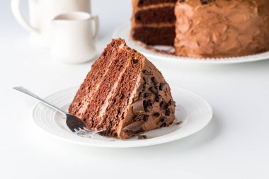 A close up of a large slice of triple layered decadent chocolate cake, ready for eating.