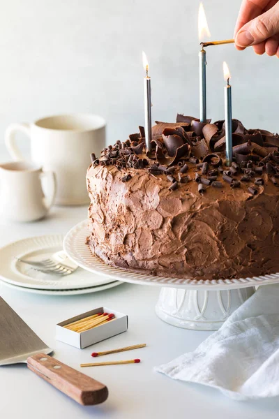 Close up of a hand lighting candles on a large homemade decorated chocolate cake. 
