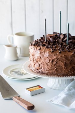 A large frosted and decorated homemade chocolate cake with candles ready for lighting. 