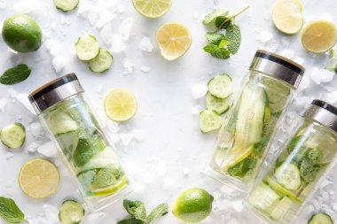 Bottles of infused cucumber water with ingredients and ice all around and copy space in the middle.