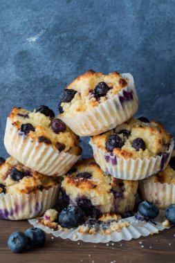 A small pile of freshly homemade blueberry muffins against a blue background. 