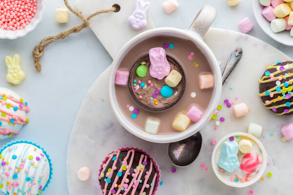 A look into a mug of hot cocoa with a hot chocolate bomb floating, surrounded by more hot cocoa bombs.