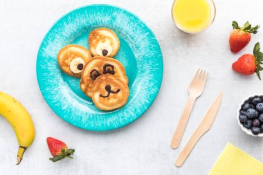 Pancakes in the shape of a bear for kids breakfast, served with fruit and juice. 