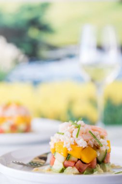 Fresh crab and shrimp stack salad garnished with chives and served with white wine, against a soft focus background.